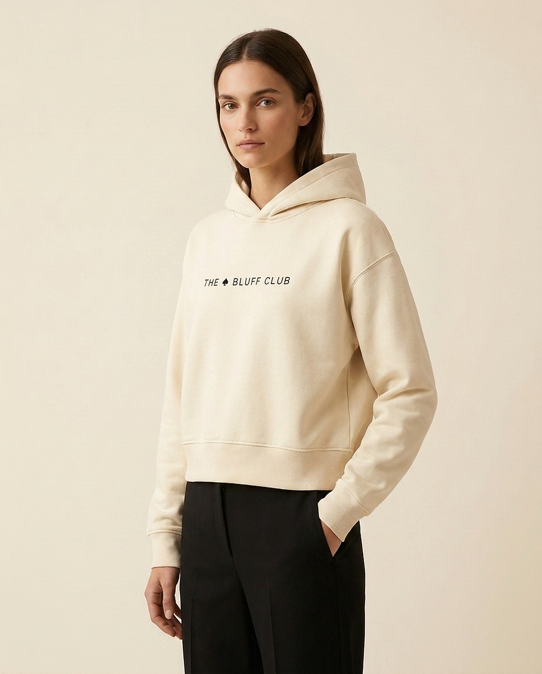 Modèle portant le hoodie cropped crème The Bluff Club au logo THE (pique) BLUFF CLUB, pièce de base pour une tenue de club de poker personnalisée